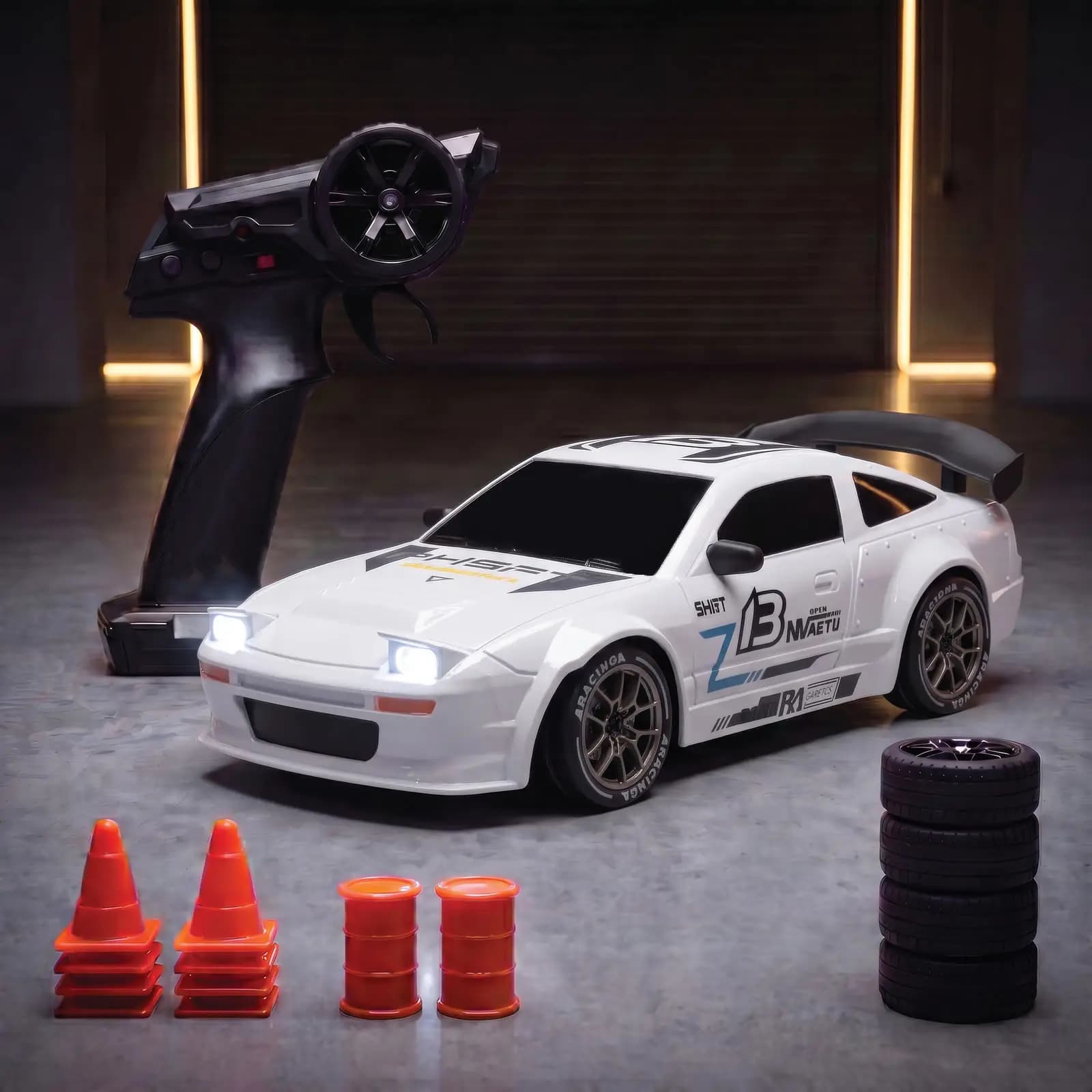 The white race coupe with a rear wing and racing decals, lights on, with the remote, spare wheels, cones and barrels